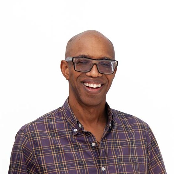 Profile photo of Andre Le Mont Wilson, a Black man with a bald head and dark-rimmed fashion glasses. He is wearing a button-up shirt in neutral tones.