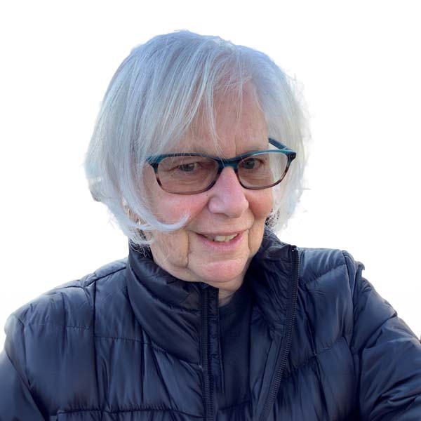 Profile image of Caryn Dickman, a White woman with chin-length white hair wearing tinted glasses and a puffy dark coat.