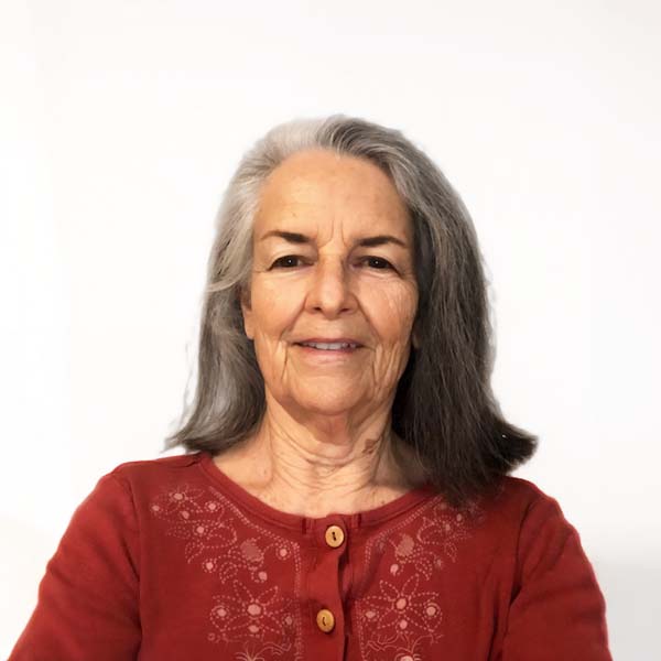 Profile image of JoAnn Lyons, a White woman with graying dark hair wearing a red cartigan.