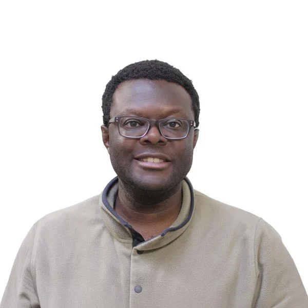 Headshot of Nana, a Black man with short black hair and glasses wearing a beige jacket.