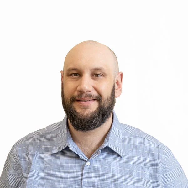 Headshot of Joseph Klobas, a man with light skin, shaved head, and a brown beard. He is dressed in a light blue collared shirt.