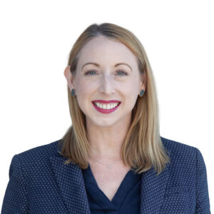 Headshot of Leslie, a smiling fair-skinned White woman with straight blonde hair wearing a blue blazer over a dark blouse.
