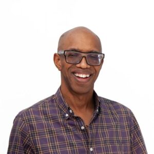 Profile photo of Andre Le Mont Wilson, a Black man with a bald head and dark-rimmed fashion glasses. He is wearing a button-up shirt in neutral tones.